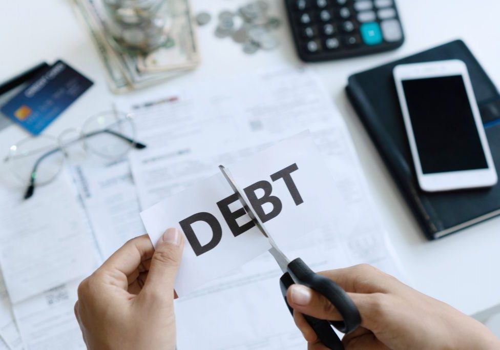 Top view of woman hands cutting of paper with the word debt written on it .